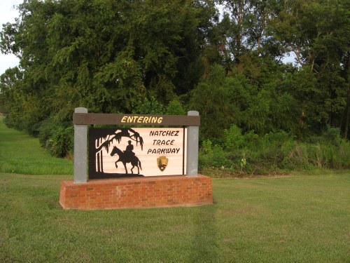 Sign marking the entrance to Natchez Trace Parkway, featuring a silhouette of a horse and rider against a natural backdrop.