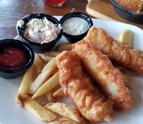 Plate of crispy fish fillets with fries, coleslaw, and dipping sauces.