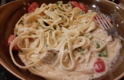 A bowl of creamy fettuccine pasta with cherry tomatoes and herbs, garnished and served with a fork.