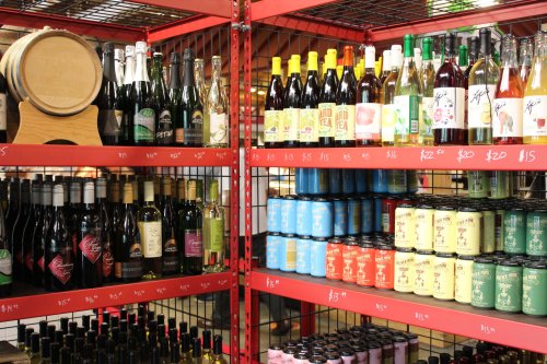 Shelves filled with various bottles of wine, sparkling drinks, and canned beverages in a retail display.