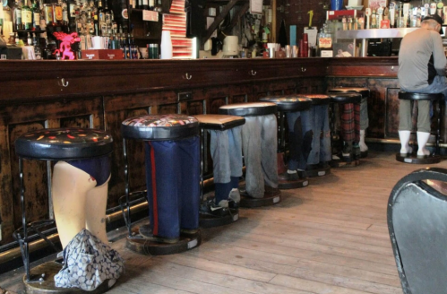 A row of bar stools with pants draped over them, creating a humorous illusion of seated patrons.