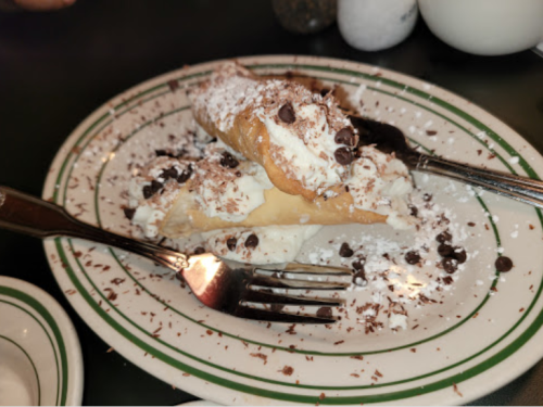 A plate of cannoli filled with cream, topped with powdered sugar and chocolate chips, with forks on the side.