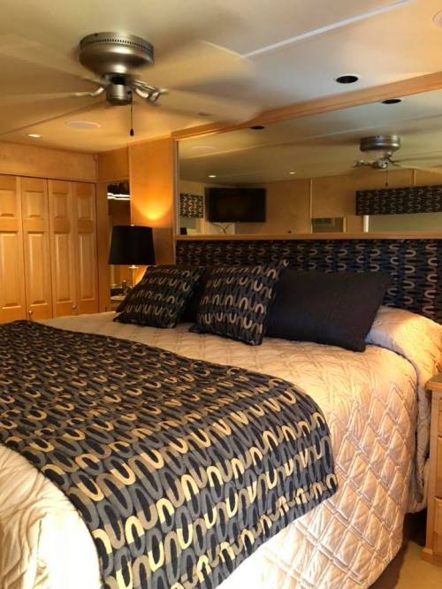 Cozy bedroom featuring a large bed with patterned bedding, a ceiling fan, and mirrored walls.