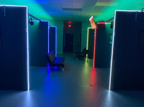 A dimly lit hallway with colorful neon-lit doorways and benches along the sides.