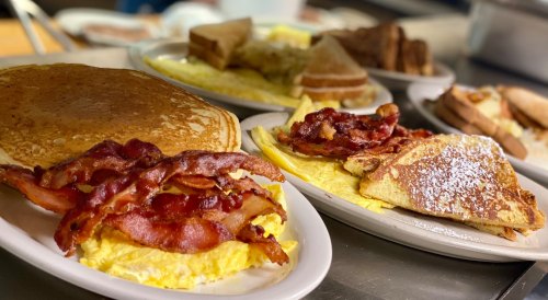 A hearty breakfast spread featuring pancakes, bacon, omelets, and French toast on white plates.