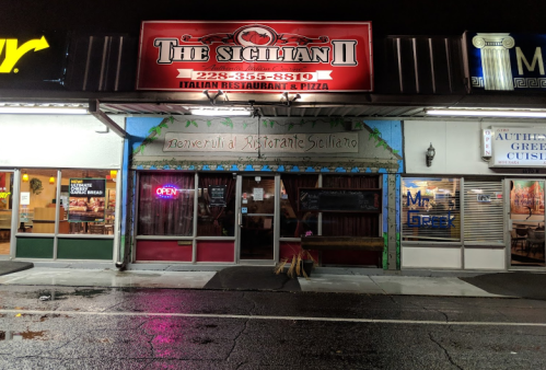 A brightly lit Italian restaurant, "The Sicilian II," with an open sign, located among other eateries at night.