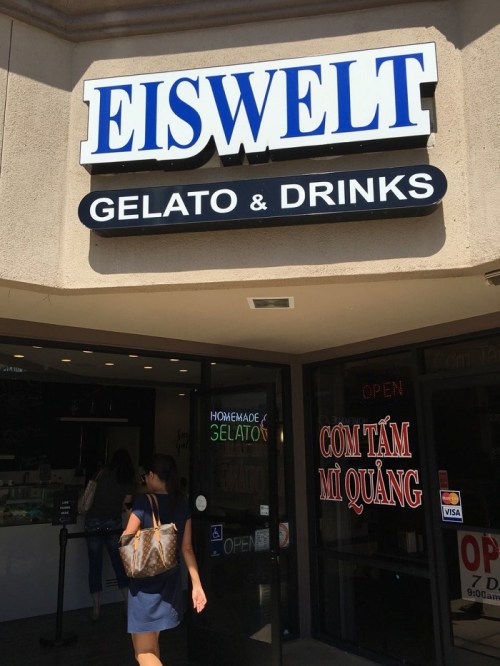 A person walks towards the entrance of Eiswelt Gelato & Drinks, featuring a sign and an open door.