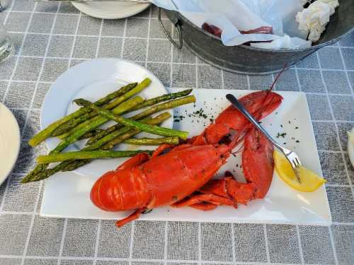 A cooked lobster on a plate with grilled asparagus and a lemon wedge, served on a checkered tablecloth.