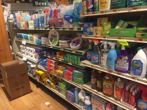 A grocery store aisle filled with various cleaning supplies, paper products, and beverages on shelves.