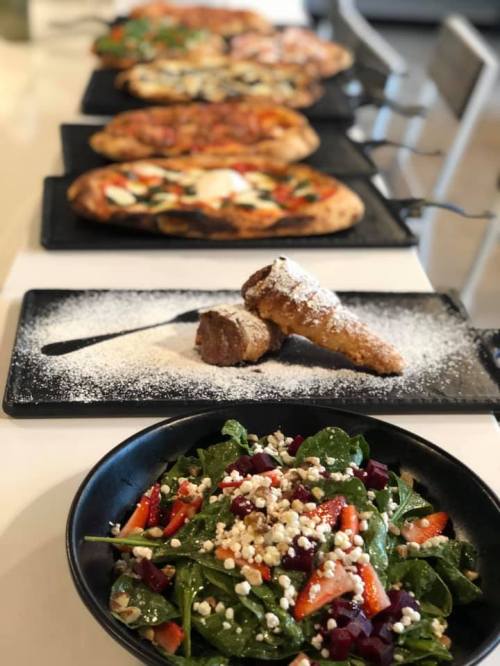 A table with a variety of pizzas and a salad in a bowl, garnished with cheese and vegetables.