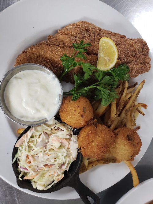 A plate featuring fried fish, coleslaw, hushpuppies, fries, and a lemon wedge, garnished with parsley.