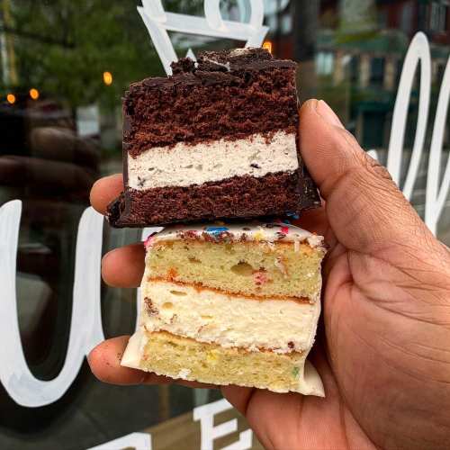 A hand holding two layers of cake: one chocolate with cream filling and one colorful vanilla with sprinkles.