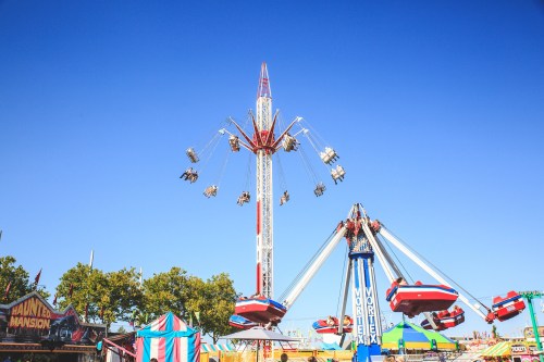 A vibrant amusement park scene featuring a tall swing ride and a spinning ride under a clear blue sky.