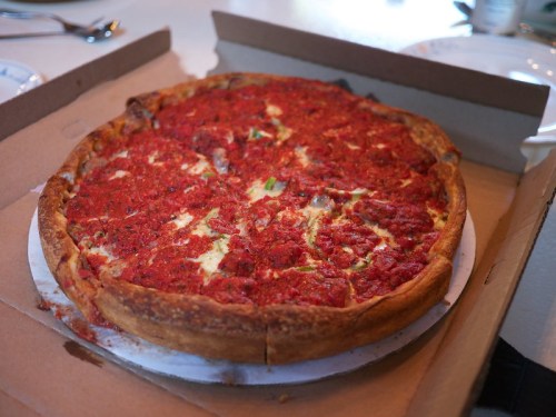 A deep-dish pizza in a cardboard box, topped with a thick layer of tomato sauce and cheese.