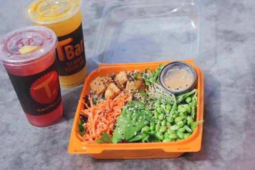 A colorful salad bowl with greens, carrots, and edamame, accompanied by two drinks in cups.