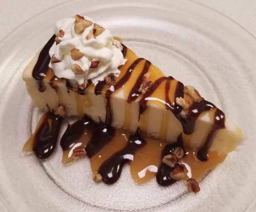 A slice of dessert topped with whipped cream, drizzled with chocolate and caramel, and sprinkled with nuts on a plate.