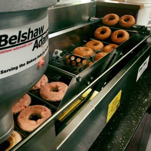 A donut fryer with freshly made donuts on a conveyor belt, labeled with "Belshaw Adamatic."