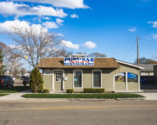 A small restaurant building with a sign reading "Pupusas Restaurant," set against a blue sky and trees.