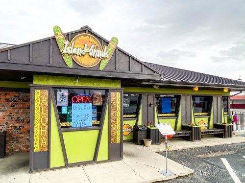Exterior of Island Grinds restaurant with a colorful sign, open windows, and a welcoming entrance.