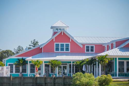 A colorful coastal house with a pink and turquoise exterior, featuring a peaked roof and palm trees in the foreground.