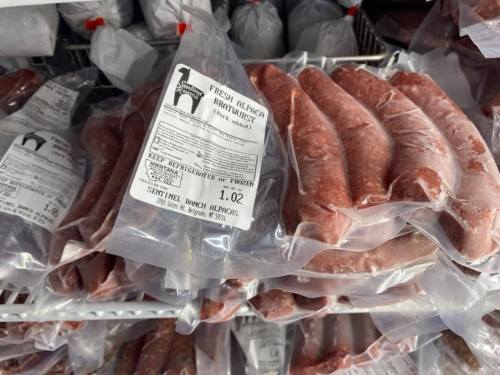 Packages of fresh sausage in clear plastic, labeled with product information, displayed in a freezer.