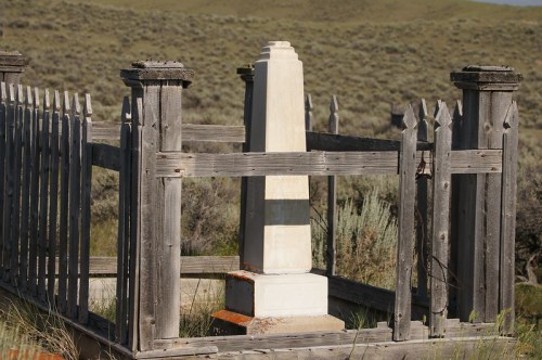 A weathered wooden fence surrounds a white monument in a grassy landscape.