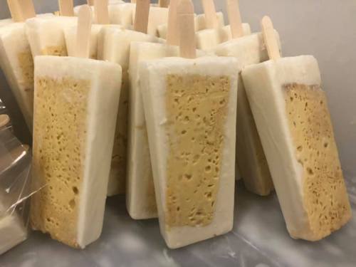 A close-up of several popsicles with a creamy exterior and a textured, yellow filling, arranged on a surface.