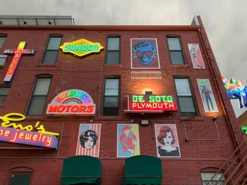 Colorful neon signs and vintage posters adorn a red brick building, creating a vibrant urban scene.