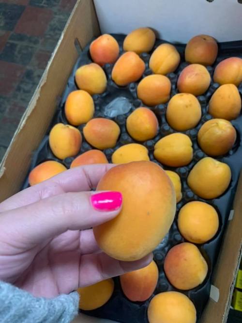 A hand holding a peach in front of a box filled with more peaches.