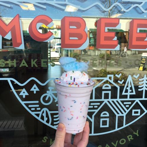 A colorful milkshake topped with blue cotton candy and sprinkles, held in front of a McBee's sign.