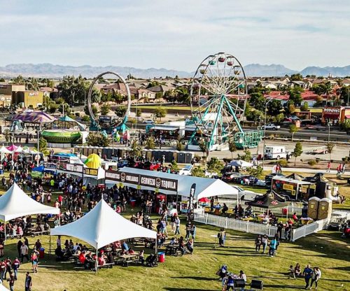 A lively outdoor fair with rides, food stalls, and crowds enjoying the festivities under a clear sky.