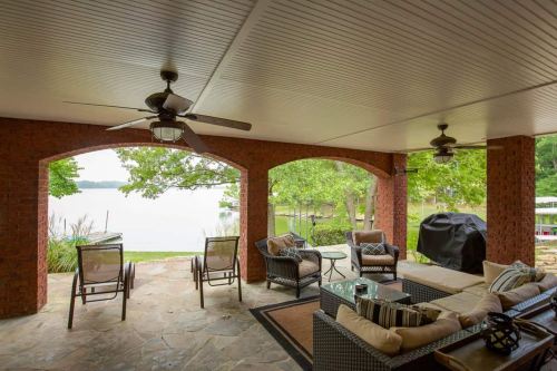 Cozy outdoor patio with seating, a table, and a view of a lake surrounded by greenery.