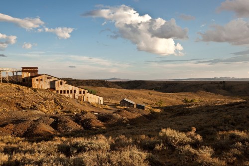 Abandoned buildings on a barren landscape under a blue sky with scattered clouds.