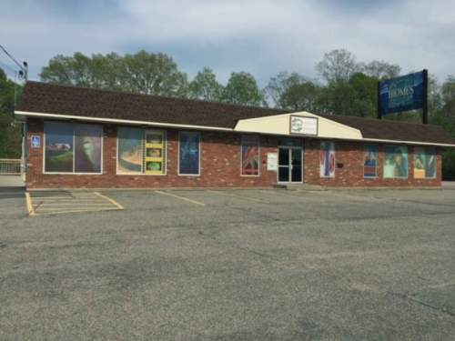 A brick building with large windows displaying colorful graphics, set in a parking lot surrounded by trees.