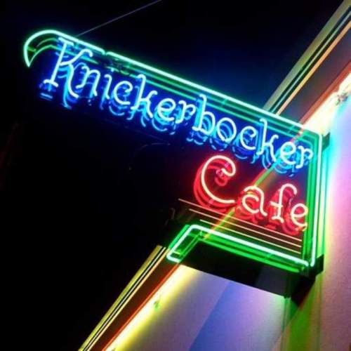 Neon sign for "Knickerbocker Cafe" glowing in vibrant colors against a dark background.