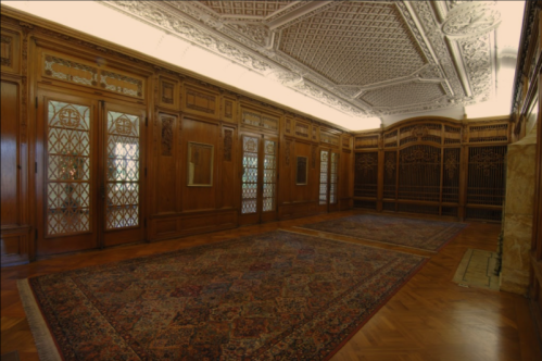 A spacious room with ornate wooden walls, intricate ceiling details, and a large patterned rug on the floor.