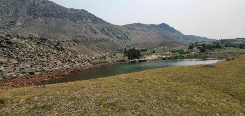 A serene landscape featuring a calm lake surrounded by rocky mountains and grassy terrain under a clear sky.