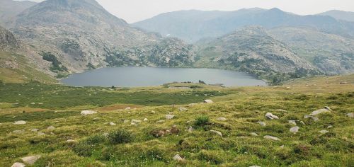 A serene mountain landscape featuring a calm lake surrounded by rocky hills and lush green meadows.