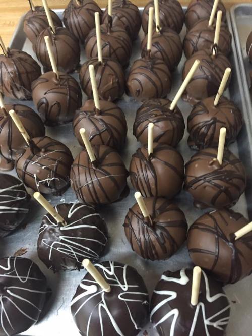 A tray of chocolate-covered caramel apples, some drizzled with white and dark chocolate, on wooden sticks.