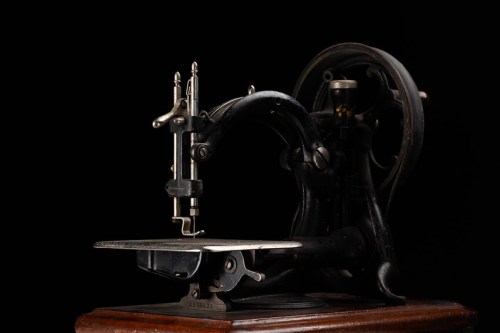 An antique sewing machine with a black metal frame and wooden base, set against a dark background.
