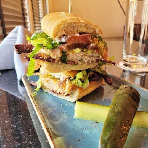 A stacked sandwich with layers of meat, lettuce, and sauce, served on a blue plate with a pickle on the side.