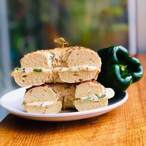 A plate with two bagel halves spread with cream cheese and green peppers, next to a whole green bell pepper.