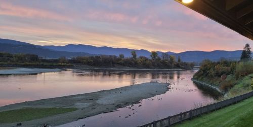 A serene river at sunset, with mountains in the background and a colorful sky reflecting on the water.