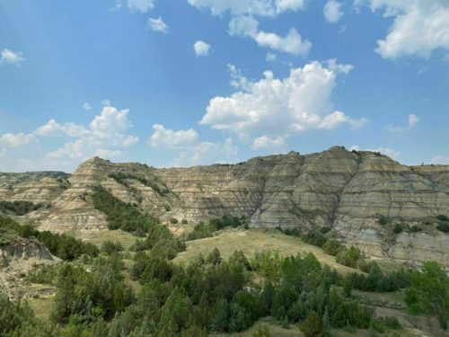 A scenic view of layered hills and green vegetation under a blue sky with scattered clouds.