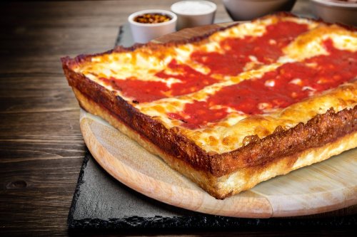 A rectangular pizza with a thick crust, topped with red sauce and melted cheese, served on a wooden board.