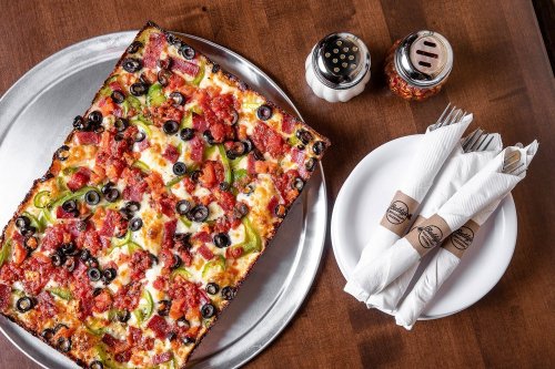 A rectangular pizza topped with pepperoni, olives, and green peppers, served with salt and pepper shakers and napkins.