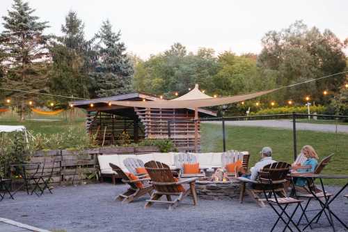 Cozy outdoor seating area with a fire pit, surrounded by trees and string lights, perfect for gatherings.