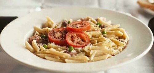 A plate of pasta with tomatoes and peas, garnished with black pepper, served on a white dish.