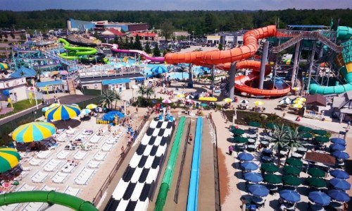 Aerial view of a vibrant water park with slides, pools, and sunbathers under colorful umbrellas.