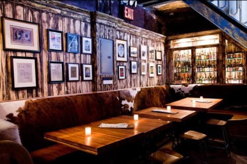 Cozy restaurant interior with wooden tables, framed art on the walls, and a well-stocked bar in the background.